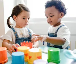 image of a boy and girl preschooler playing with stacking cups on a table.